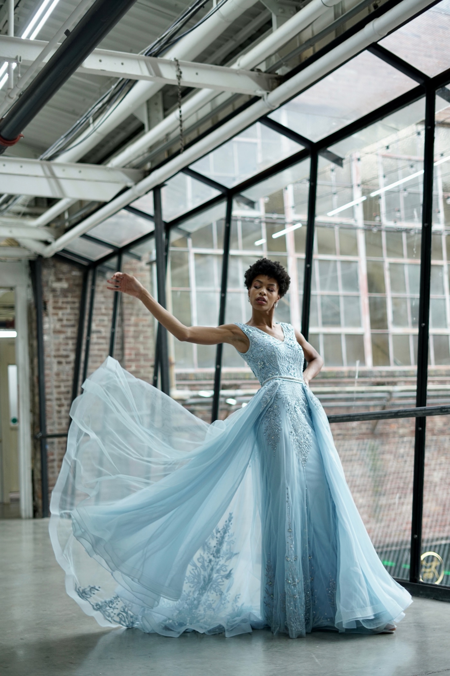 RiRi, fashion model, in a flowing powder-blue tulle couture gown caught mid-spin inside a glass-roof loft