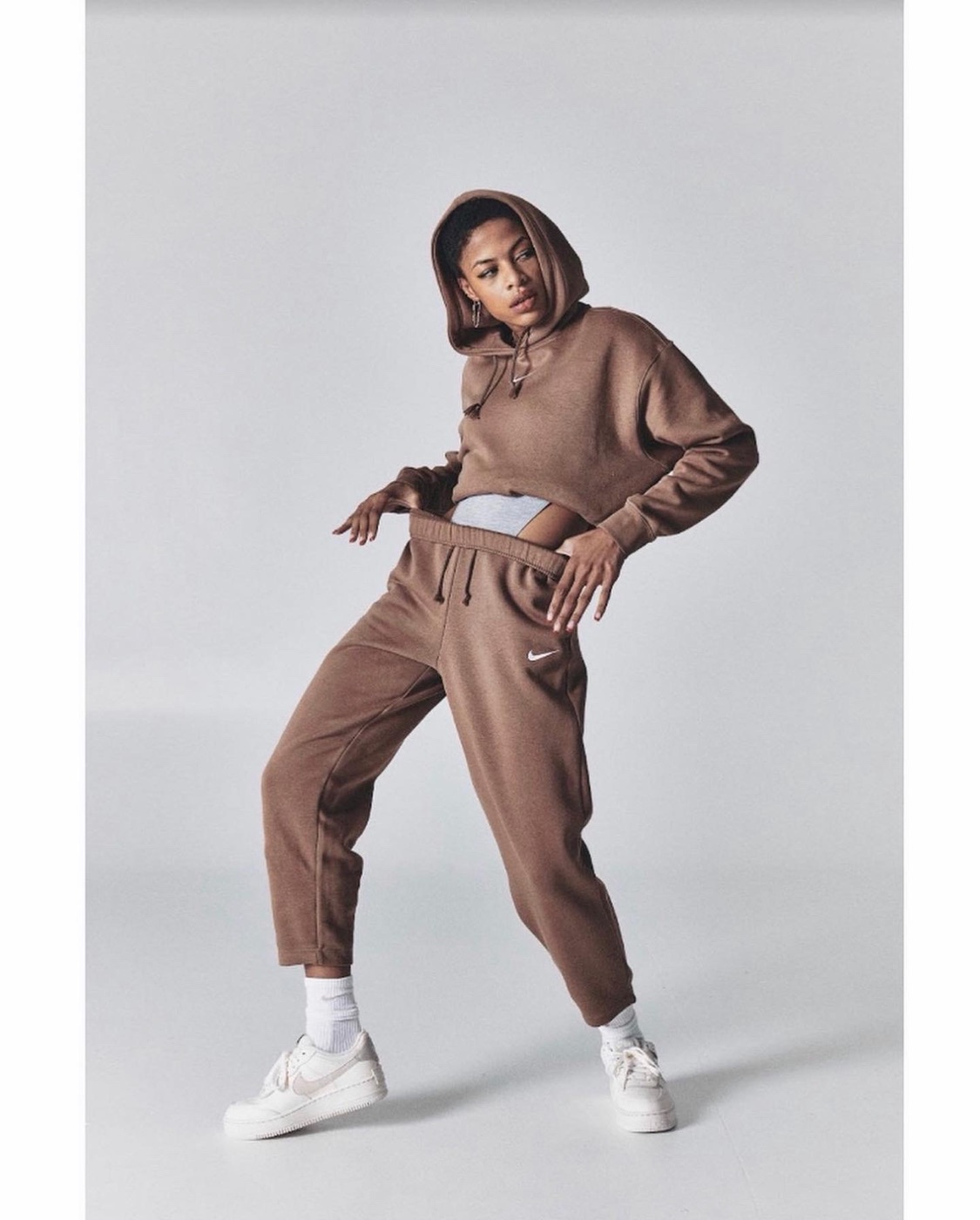 RiRi, commercial model, in a brown Nike sweatsuit and Air Force 1 sneakers, mid-motion in studio